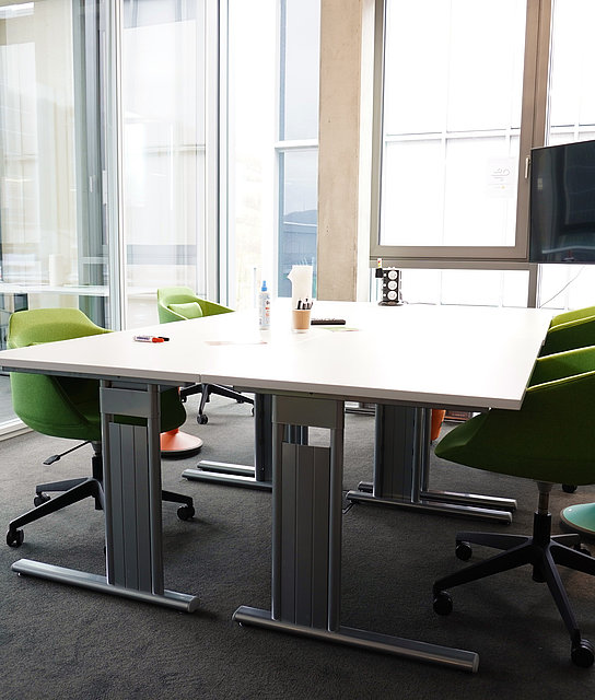 Büro mit einem Bildschirm, einer Schreibtischgruppe mit grünen Stühlen